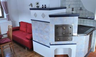 A cozy living kitchen with a modern oven and a red sofa. The room has tiled walls and plenty of natural light.