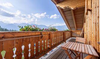 A cozy wooden balcony with a view of the mountains. Flowers adorn the railing under a clear blue sky.