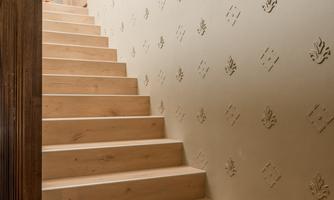 A bright wooden staircase leads to a hallway. The wall is decorated with a subtle, textured pattern.
