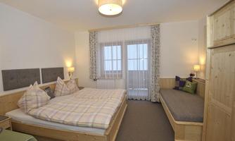 A cozy bedroom with a large double bed and wooden details. The room has a window with a view and a seating area.