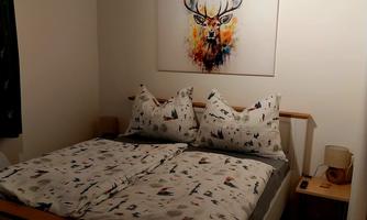 A cozy bedroom with a double bed and colorful bedspreads. On the wall hangs a picture of a raging deer.