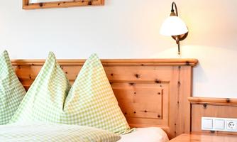 A cozy bedroom with a wooden bed and checked pillows. On the wall hangs a picture of a mountain landscape.