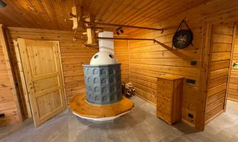 A cozy room with wooden paneling and a traditional stove in the center. A door and a cabinet are also visible.