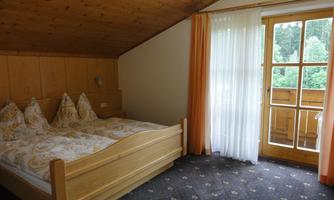 A cozy bedroom with a double bed and light curtains.  
Windows overlooking the outside provide plenty of daylight.