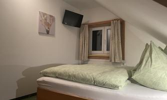 A cozy bedroom with a bed and green pillows. A picture hangs on the wall and a television is mounted.
