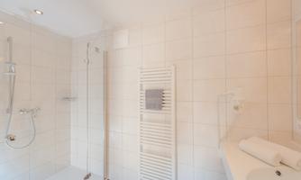 A modern bathroom with a shower and bright tiles. Towels and accessories are neatly arranged.