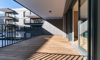 A modern balcony with a wooden floor. In the background, modern buildings can be seen.