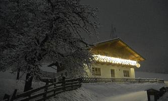 A snow-covered house under a dark sky. The facade is adorned with lights that create a cozy atmosphere.