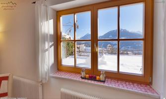 A cozy window with a view of snow-covered mountains and a clear, blue sky. On the windowsill are some decorative elements.