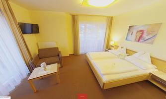 A cozy hotel room with two beds, a television, and a small table. The walls are painted in warm shades of yellow, and large windows let in plenty of light.