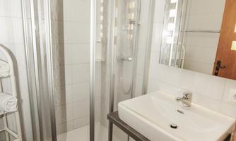 A modern bathroom with a clear shower cabin and an elegant sink. Towels are neatly stacked and there is a wooden cabinet.