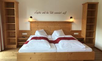 A cozy bedroom with a double bed and a wooden frame. There are shelves on the walls and a decorative wall inscription.