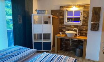 A cozy bedroom with two beds and a modern sink. The decor is bright and friendly, with wood and stone accents.