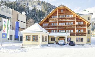 A cozy hotel in the snow with a beautiful wooden facade. In the background, snow-covered mountains can be seen.