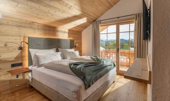 A cozy bedroom with a double bed and modern wooden elements. Large windows provide a view of the mountains and let in plenty of daylight.