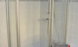 A modern shower with transparent glass doors and gray tiles. A red towel is on the shower shelf.