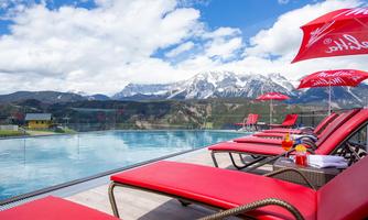 A luxurious pool with red loungers and a view of snow-capped mountains. The sky is clear and the atmosphere is inviting.