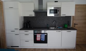 A modern kitchen with white cabinets and a dark countertop. It is equipped with a stove, a microwave, and a sink.