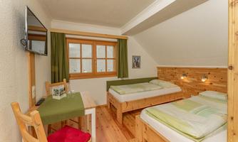 A cozy room with two single beds and a wooden table. Large windows let in a lot of light, and the decor is simple and modern.