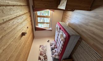 A cozy bedroom with a double bed and wooden ceiling. There is a window with curtains and a television in a wooden cabinet.