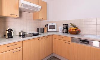 A modern kitchen with wooden cabinets and a bright, friendly atmosphere. Kitchen utensils and a bowl of fresh fruit are on the countertop.
