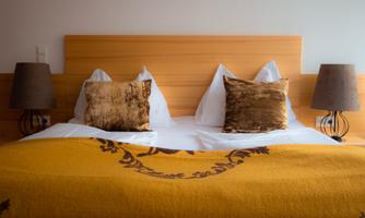 A cozy hotel room with a large bed, decorative pillows, and a warm blanket. Next to the bed are two table lamps.