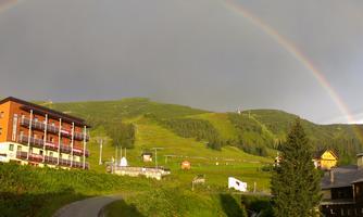 A colorful rainbow over a green valley. In the foreground, you can see several cozy buildings.