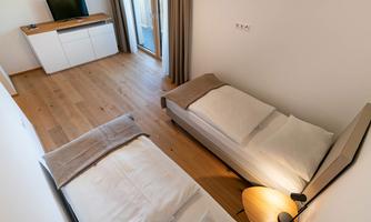 A modern room with two single beds and wooden flooring. There is a cozy lamp lighting and a desk area.