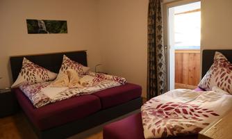 A modern bedroom with two beds decorated with colorful bedspreads. The room has a balcony and plenty of daylight.
