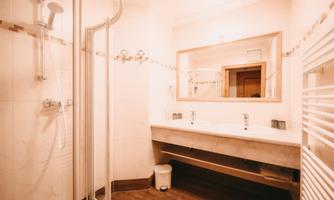 A modern bathroom with a shower, sink, and mirror. The walls are light and the floor is wooden.