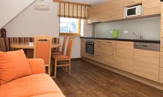 A bright and modern kitchen with wooden cabinets and an orange sofa. The space is designed to be friendly and inviting.