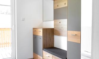 A modern hallway with a wooden wardrobe and gray doors. The room is bright and inviting, with access to a balcony.