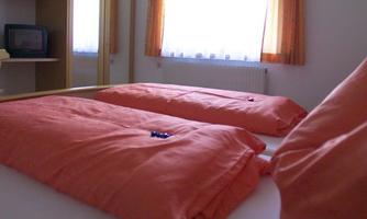 A cozy bedroom with a double bed and orange bedcovers. The room has large windows that let in plenty of daylight.