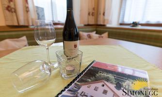 On the table lies a bottle of wine, two wine glasses, and a book about the holiday home Simonegg. The table is set with a light cloth, creating a cozy atmosphere.