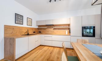 A modern kitchen with light cabinets and a wooden countertop. The floor is made of wood and there is a dining table with chairs.