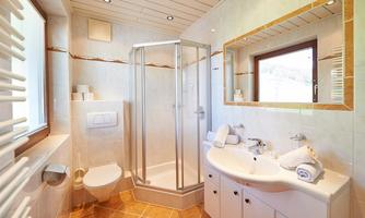 A modern bathroom with a shower, sink, and elegant tiles. It is bright and well-lit, with a window for daylight.