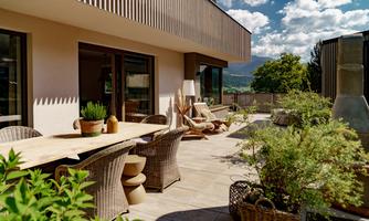 A stylish terrace with modern furniture and green plants. In the background, gentle hills and a blue sky can be seen.