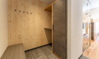 A modern entrance area with wooden paneling and a simple seating area. Some hooks are hanging on the wall, and there is a functional wardrobe.