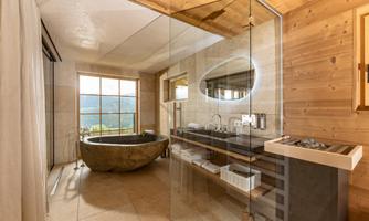 A modern bathroom with large windows and a view of nature. The amenities include a unique stone bathtub and an elegant wash area.