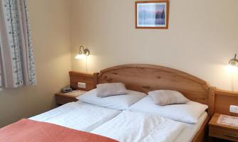 A cozy bedroom with a double bed and an orange blanket. There is pleasant lighting and a window with curtains.