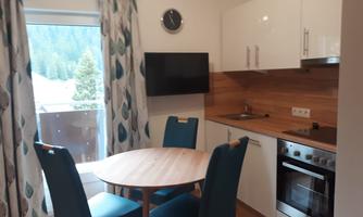 A modern kitchen with a round table and blue chairs. The view of nature through the window completes the atmosphere.