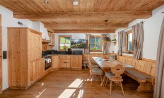 A cozy kitchen with wooden interiors and a large dining table. Bright windows offer a view of the landscape.
