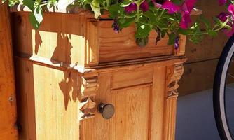 An elegant wooden flower box with colorful petunias in purple and white colors. The box stands in front of a wooden cladding and gives the surroundings a fresh look.