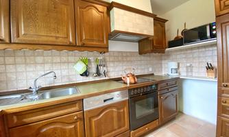 A modern kitchen with wooden cabinets and bright tiles. The equipment includes a stove, a refrigerator, and various kitchen utensils.