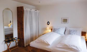 A bright and cozy bedroom with a large bed and decorative pillows. A mirror and a wooden wardrobe complete the room.