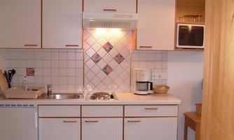 A bright and modern kitchen with white furniture. It includes a sink, a stove, and a coffee machine.