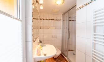 A modern bathroom with a shower and a sink. The walls are tiled and there is plenty of natural light.