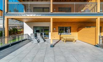 A modern terrace with wooden cladding and a dining area. There are several loungers and a bright, open space.