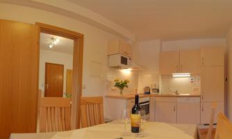 A modern kitchen with wood details and a dining table group. On the table is a bottle of wine and fresh flowers.