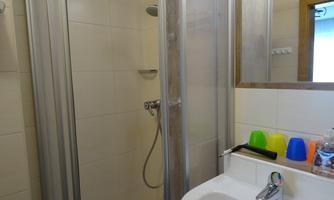 A small bathroom with a shower and a sink. Colorful plastic cups are placed next to the sink.